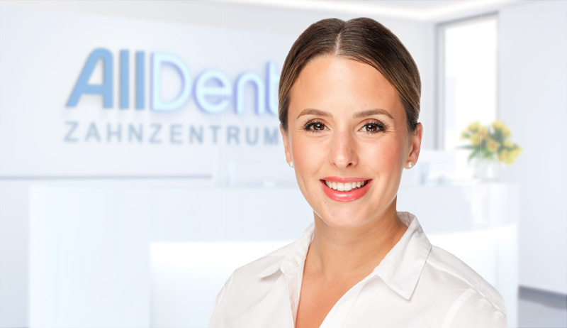 Freundliche Zahn&auml;rztin l&auml;chelt in die Kamera, im Hintergrund der Empfangsbereich der Praxis