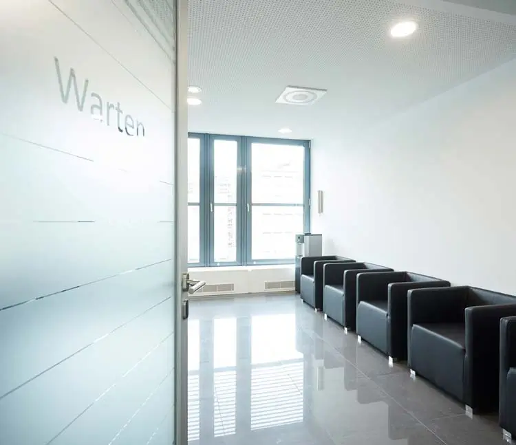 Helles Wartezimmer mit dunklen Ledersesseln und grauen Fliesen