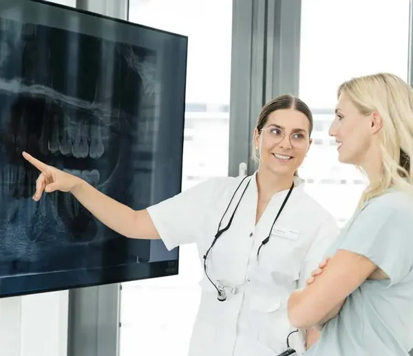 Zahnärztin erklärt einer Patientin ihr Röntgenbild am Bildschirm und zeigt auf das Bild