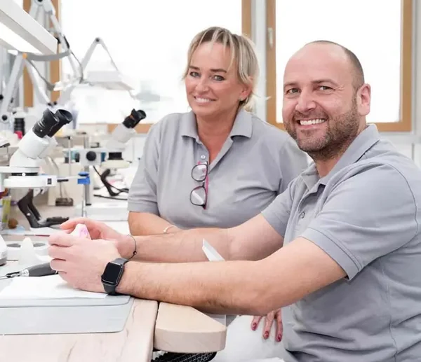 Zwei Labortechniker sitzen an ihren Arbeitsplätzen und lächeln in die Kamera